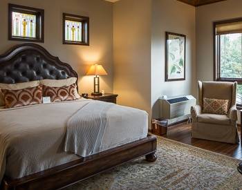 Wood platform bed with leather Headboard lined in brown wood. One tan high back chair and an view of the mountains out the window.
